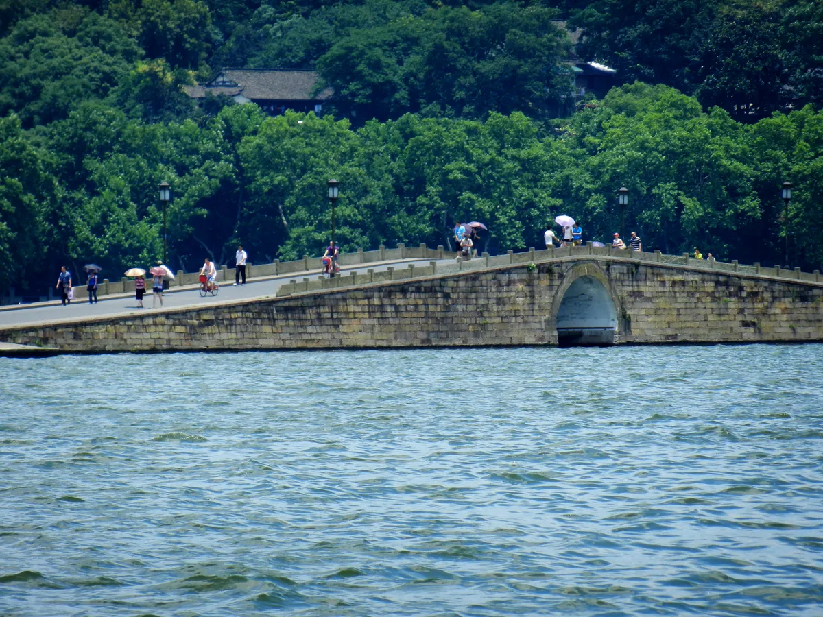 People crossing a stone bridge on Bai Causeway at West Lake in Hangzhou