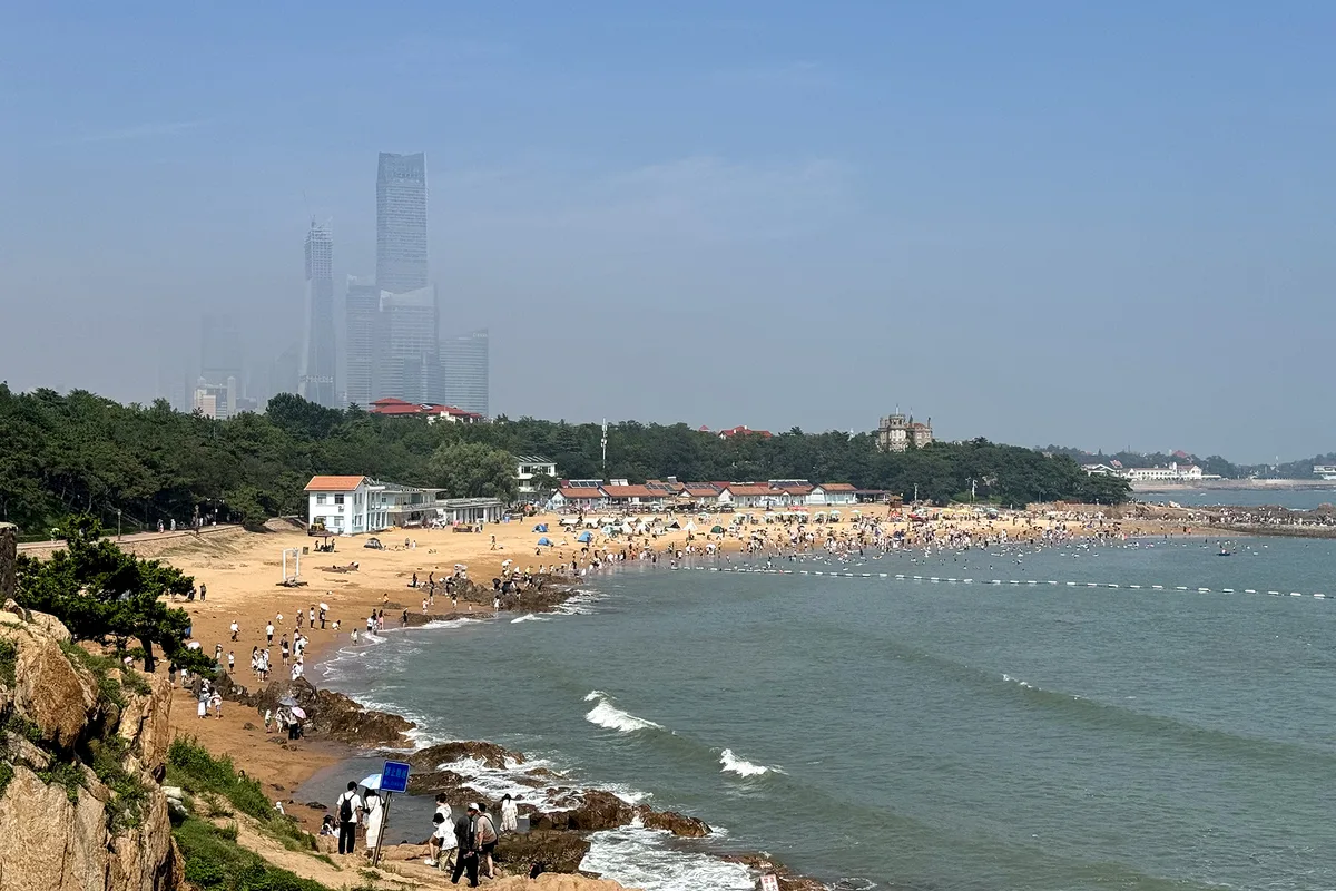 Sandy beach and shoreline near Badaguan in Qingdao with distant towers across the haze