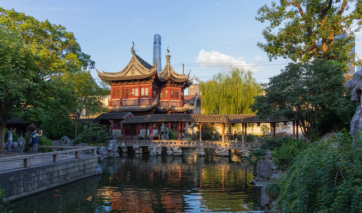 Pavilion and covered walkway over a pond inside Yu Garden in Shanghai, with a modern tower in the distance
